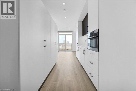 A long, narrow, white hallway with a kitchen area at the end.