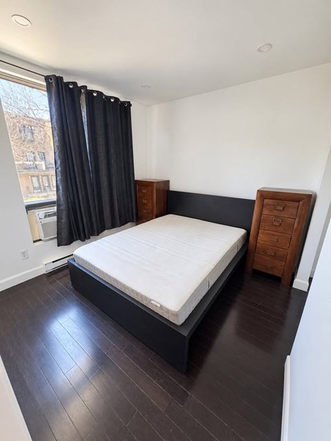 A bedroom with a bed, nightstand, and window with black curtains.