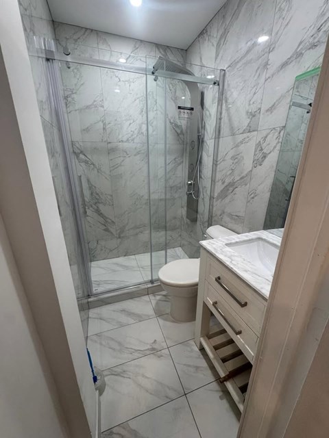 A bathroom with a marble tile floor and walls, a toilet, a sink, and a walk-in shower.