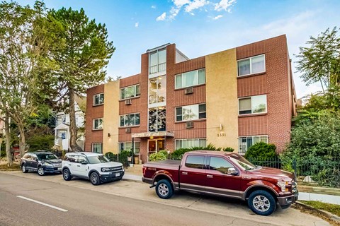 A red pickup truck is parked in front of a multi-story apartment building.