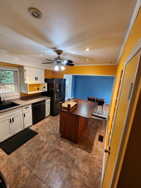 A kitchen with a brown tile floor and a ceiling fan.