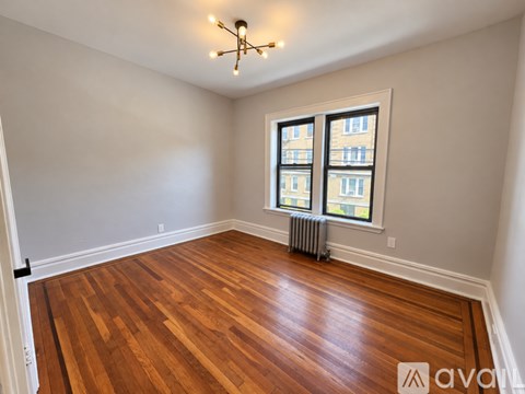 A room with wooden floors and a window with a view of a building across the street.