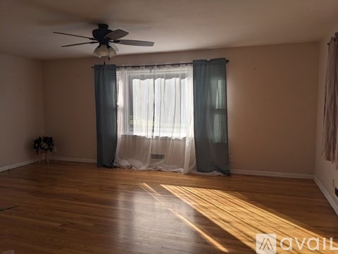 A room with a fan, curtains, and a vase on the floor.