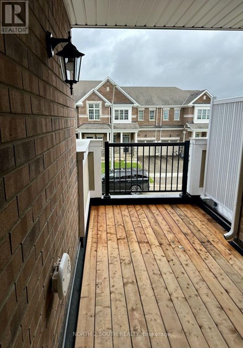 A wooden deck with a black railing and a brick wall.