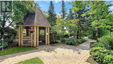 A gazebo is surrounded by a brick walkway and greenery.