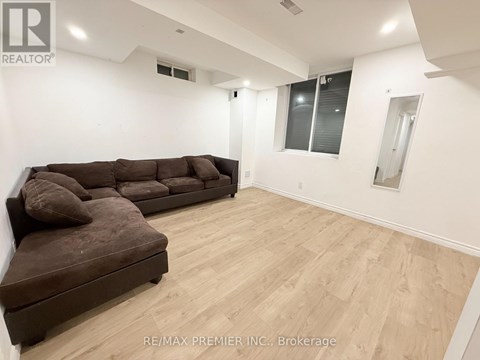 A large brown couch sits in a spacious room with wooden flooring and white walls.
