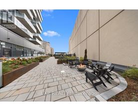 A patio with a fire pit and chairs is surrounded by a wall and a building.