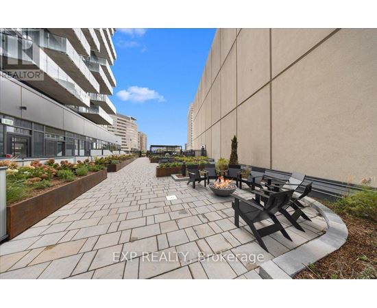 A patio with a fire pit and chairs is surrounded by a wall and a building.
