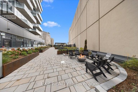 A patio with a fire pit and chairs is surrounded by a wall and a building.