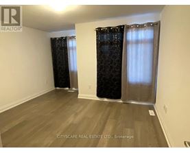 A room with wooden flooring and two windows with curtains.