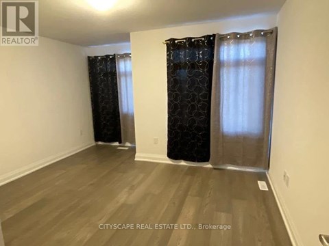 A room with wooden flooring and two windows with curtains.