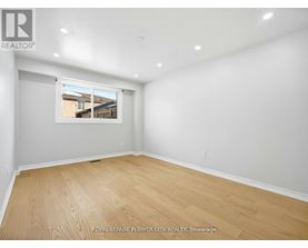A room with wooden flooring and a window showing a view of a house.