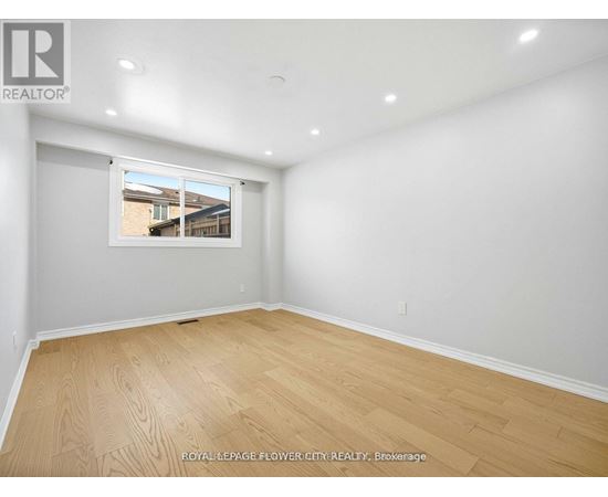 A room with wooden flooring and a window showing a view of a house.