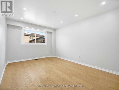 A room with wooden flooring and a window showing a view of a house.