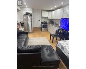 A black leather couch sits in a kitchen with white cabinets and a refrigerator.