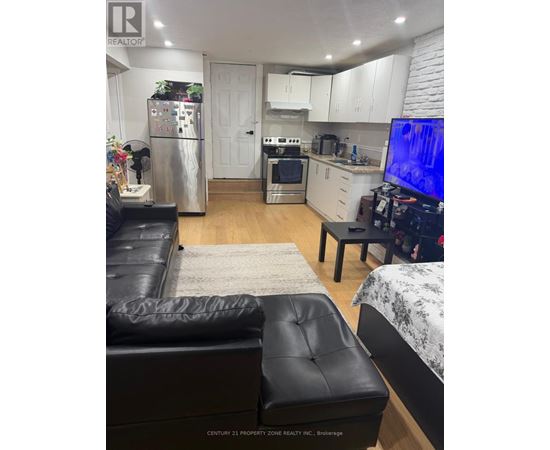 A black leather couch sits in a kitchen with white cabinets and a refrigerator.