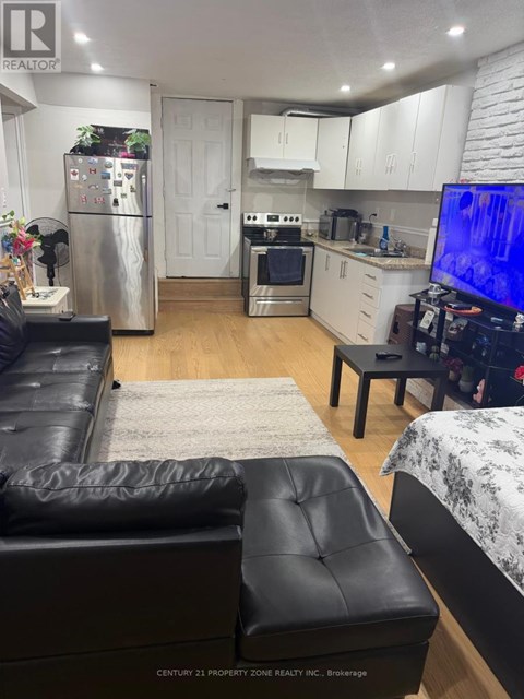A black leather couch sits in a kitchen with white cabinets and a refrigerator.