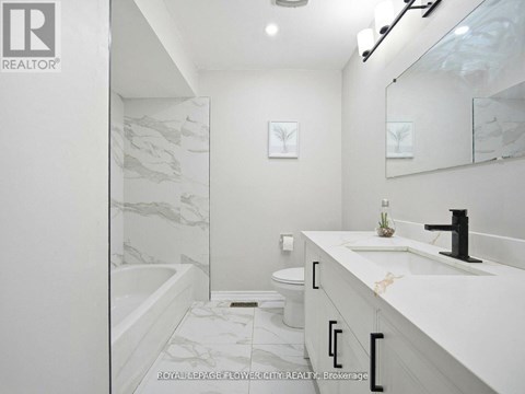 A white bathroom with a marble patterned tub and sink.