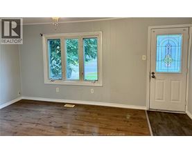 A room with a wooden floor, a white door, and a window with a view of the outside.