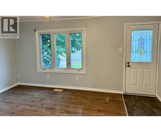 A room with a wooden floor, a white door, and a window with a view of the outside.