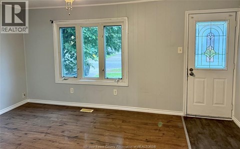 A room with a wooden floor, a white door, and a window with a view of the outside.