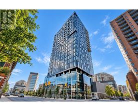 A modern glass building stands tall in a cityscape with other buildings and trees around it.