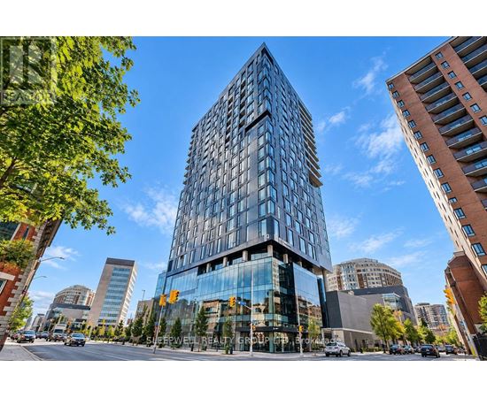 A modern glass building stands tall in a cityscape with other buildings and trees around it.