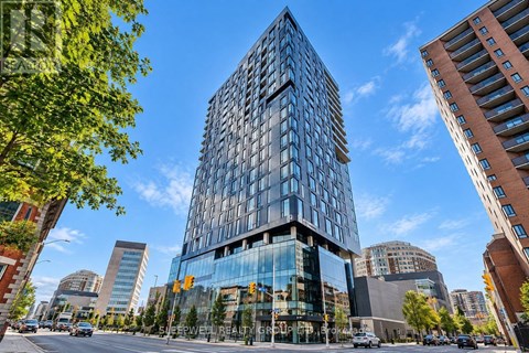 A modern glass building stands tall in a cityscape with other buildings and trees around it.