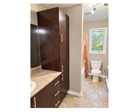 A bathroom with a toilet, sink, and cabinets.