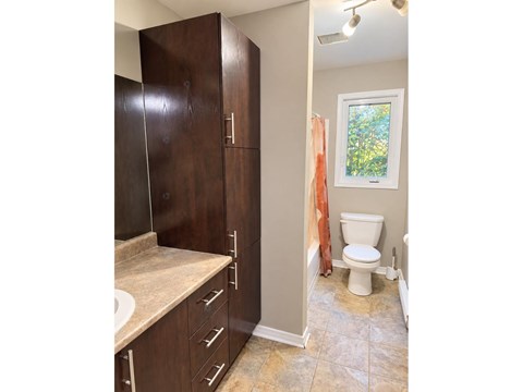 A bathroom with a toilet, sink, and cabinets.