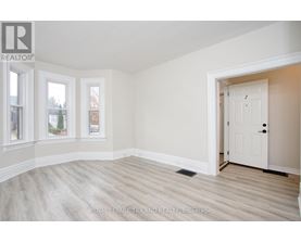 A white door is in a room with white walls and wood flooring.