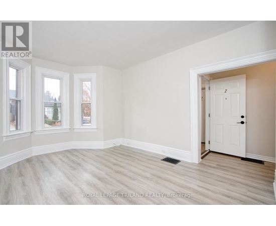 A white door is in a room with white walls and wood flooring.
