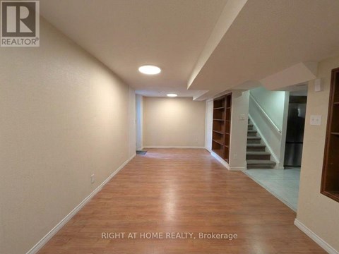 A spacious room with wooden flooring and a staircase in the background.