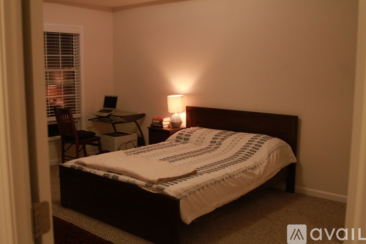 A bedroom with a bed, desk, chair, and a lamp.