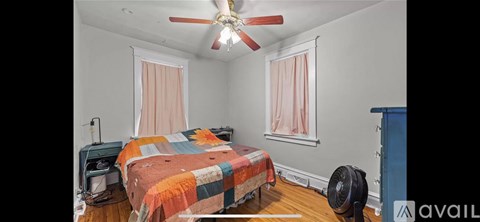 A bedroom with a bed covered in a quilt and a ceiling fan.