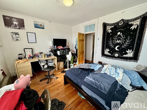 A bedroom with a bed, desk, chair, and a large tapestry hanging on the wall.