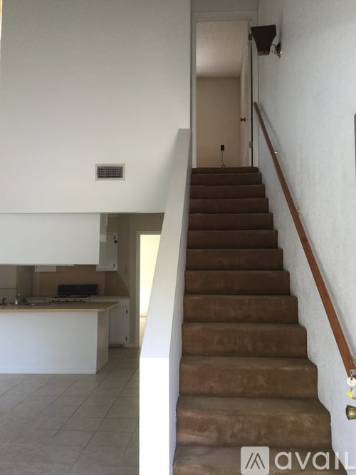 A staircase with a brown carpeted runner leads up to a white door.