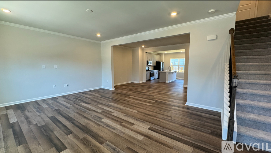A spacious room with wooden flooring and a staircase on the right side.