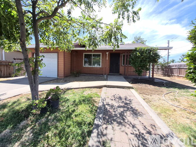 A house with a brown roof and a white garage door is surrounded by a fence and a tree.