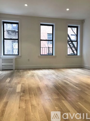 A room with wooden flooring and two windows.