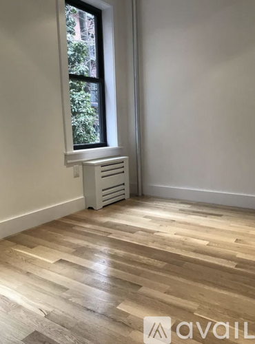 A room with wooden flooring and a window with a radiator beneath it.