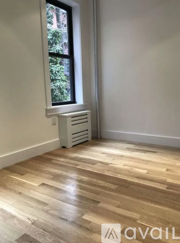 A room with wooden flooring and a window with a radiator beneath it.