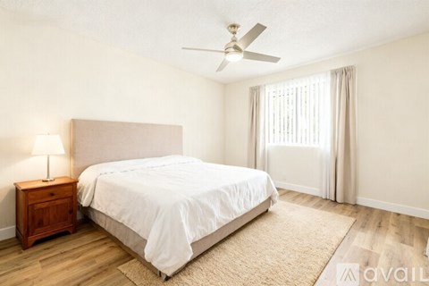 A bedroom with a large bed, a wooden nightstand, and a ceiling fan.