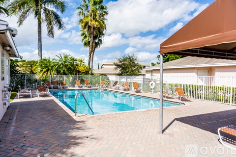 A pool surrounded by palm trees and a patio area.