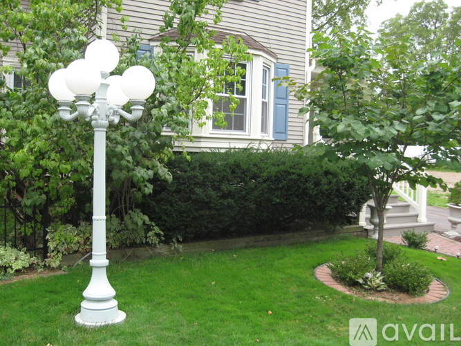 A white lamp post with six lights stands in a grassy area.