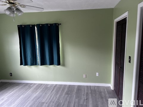 A room with a ceiling fan and a window with blue curtains.