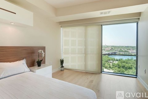 A bedroom with a large bed and a view of the city through a sliding glass door.