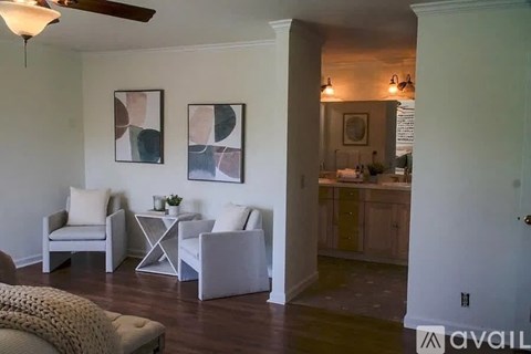 A living room with a white couch and a white chair with a painting on the wall.