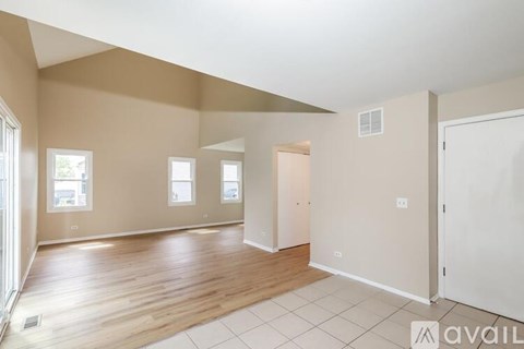 A spacious room with wooden floors and white walls, featuring a large window and a door.