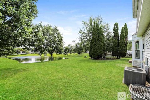A well-maintained lawn with a pond and trees in the background.